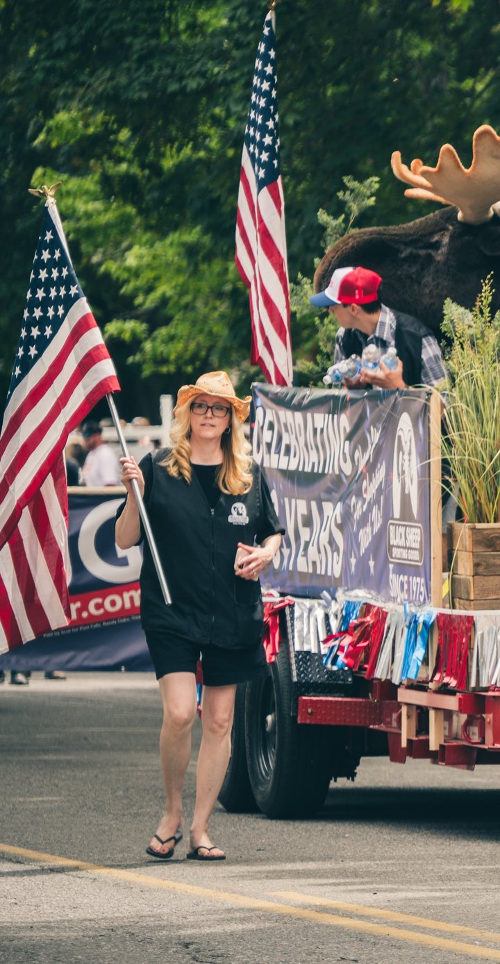 Black Sheep team member carrying an American flag beside the Celebrating 50 Years parade float.