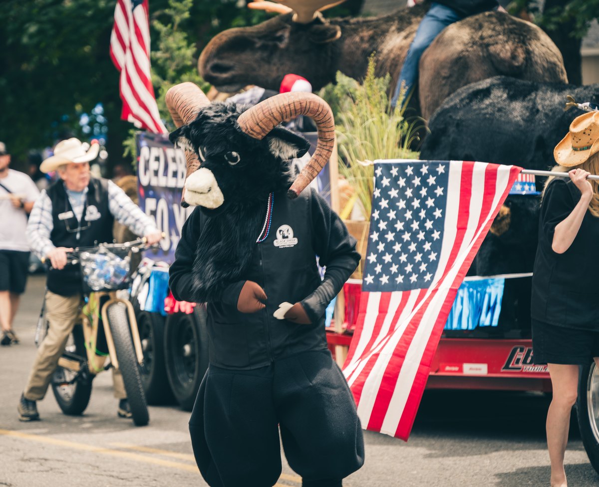 Black Sheep ram mascot walking in a parade beside the Celebrating 50 Years float and American flags.